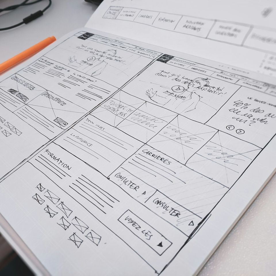 A website wireframe sketched by hand, with an orange pen beside it.