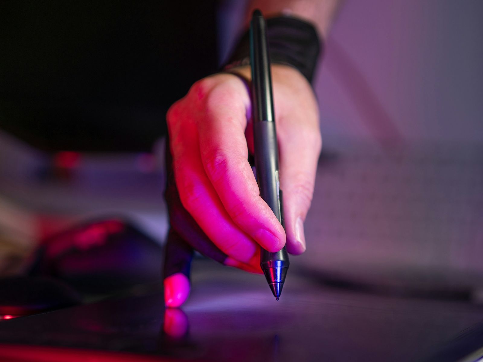 A hand drawing with a stylus on a graphics tablet in pink and violet light.