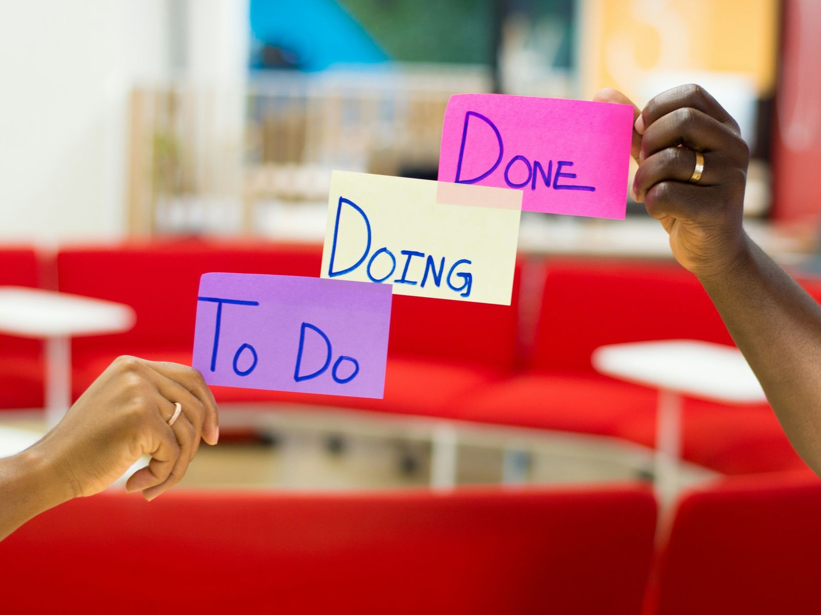 Two hands holding up three sticky notes that read To Do, Doing and Done.