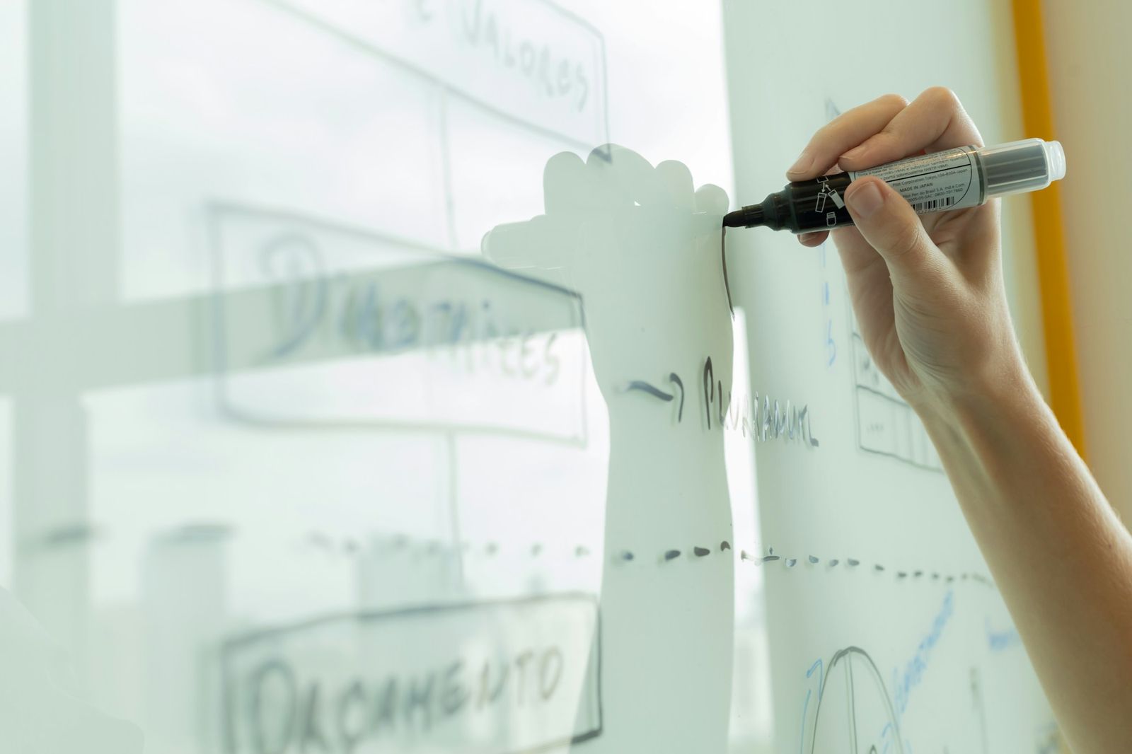 A hand drawing a diagram on a glass whiteboard.