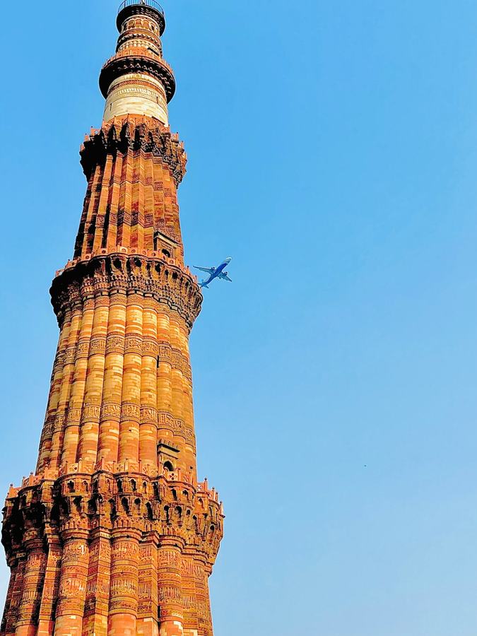 An aircraft passing the Qutub Minar against a clear blue sky.