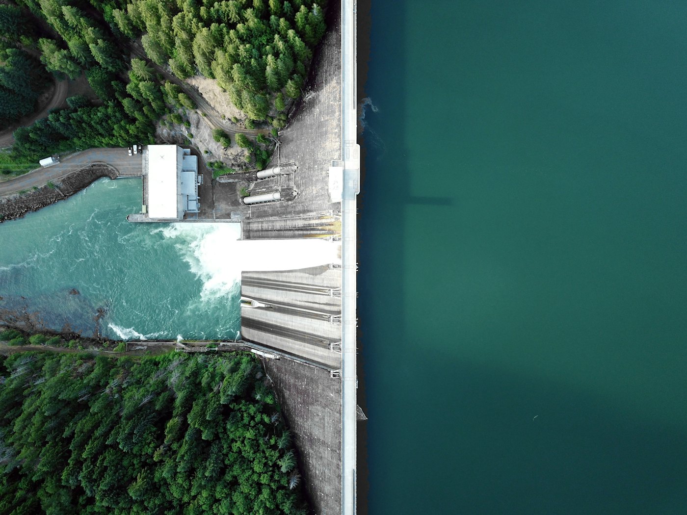 A dam spillway from directly above, with the reservoir on one side and the outflow on the other