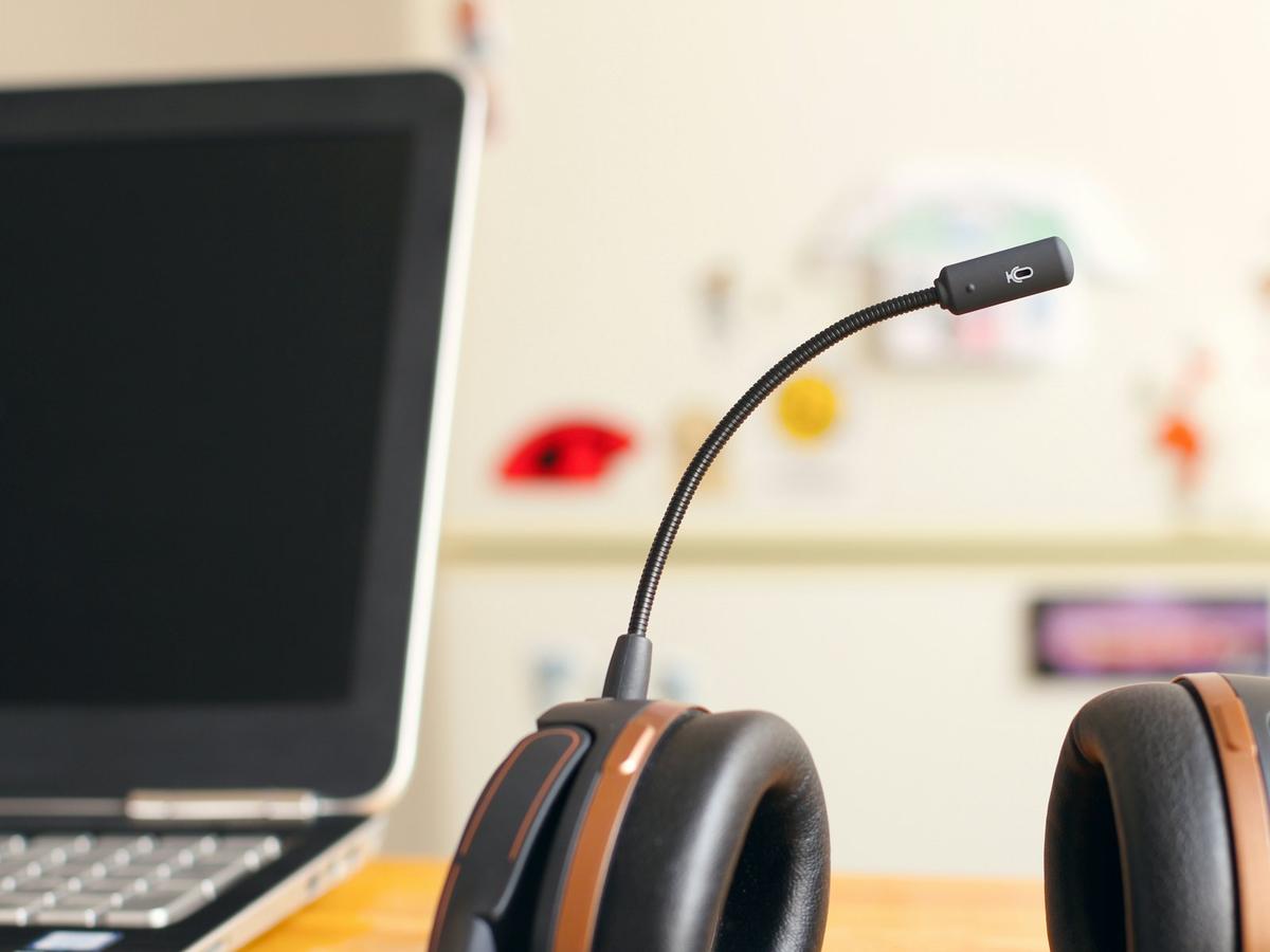 A headset with a microphone rests beside an open laptop on a desk