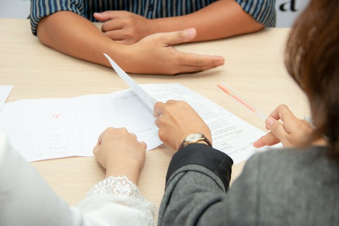Two people at a table reading printed pages, one holding a pen