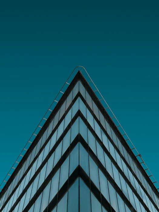 The corner of a glass office building against a deep sky, its lines converging upward