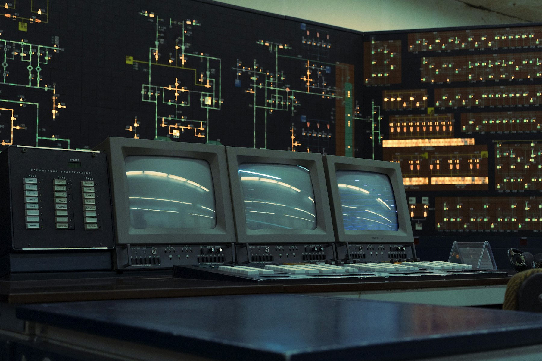 An old control room with rows of switch panels, a wall-sized system diagram and three boxy monitors