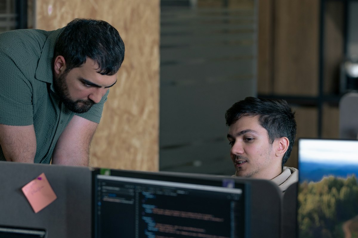 Two engineers talk through code on a monitor at a shared desk