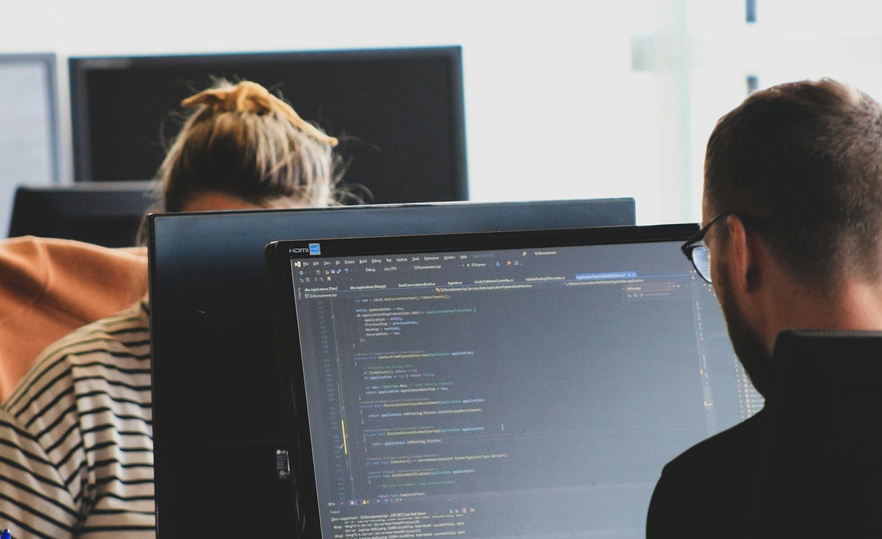 Two engineers at their desks, one reading code in an editor on a large monitor