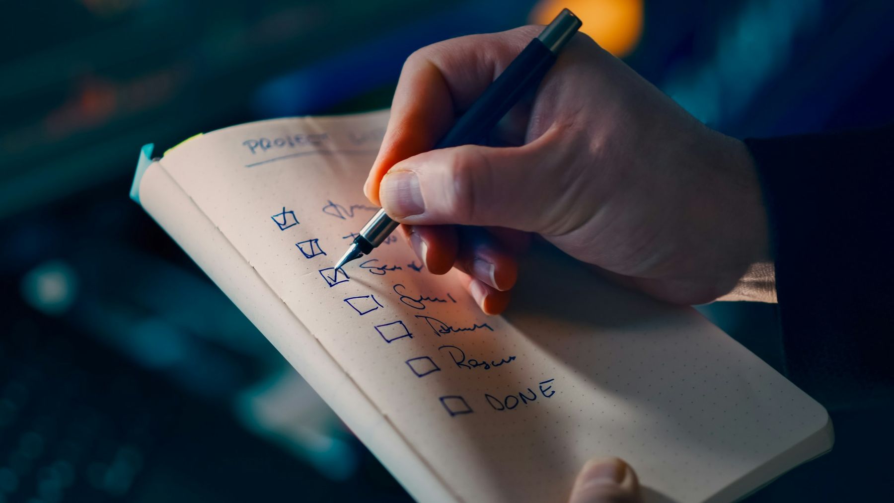A hand ticking items on a handwritten checklist in a notebook