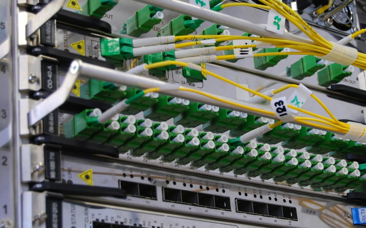 Close-up of a network chassis: rows of green fibre-optic ports with yellow patch cables, each cable tagged with a handwritten number