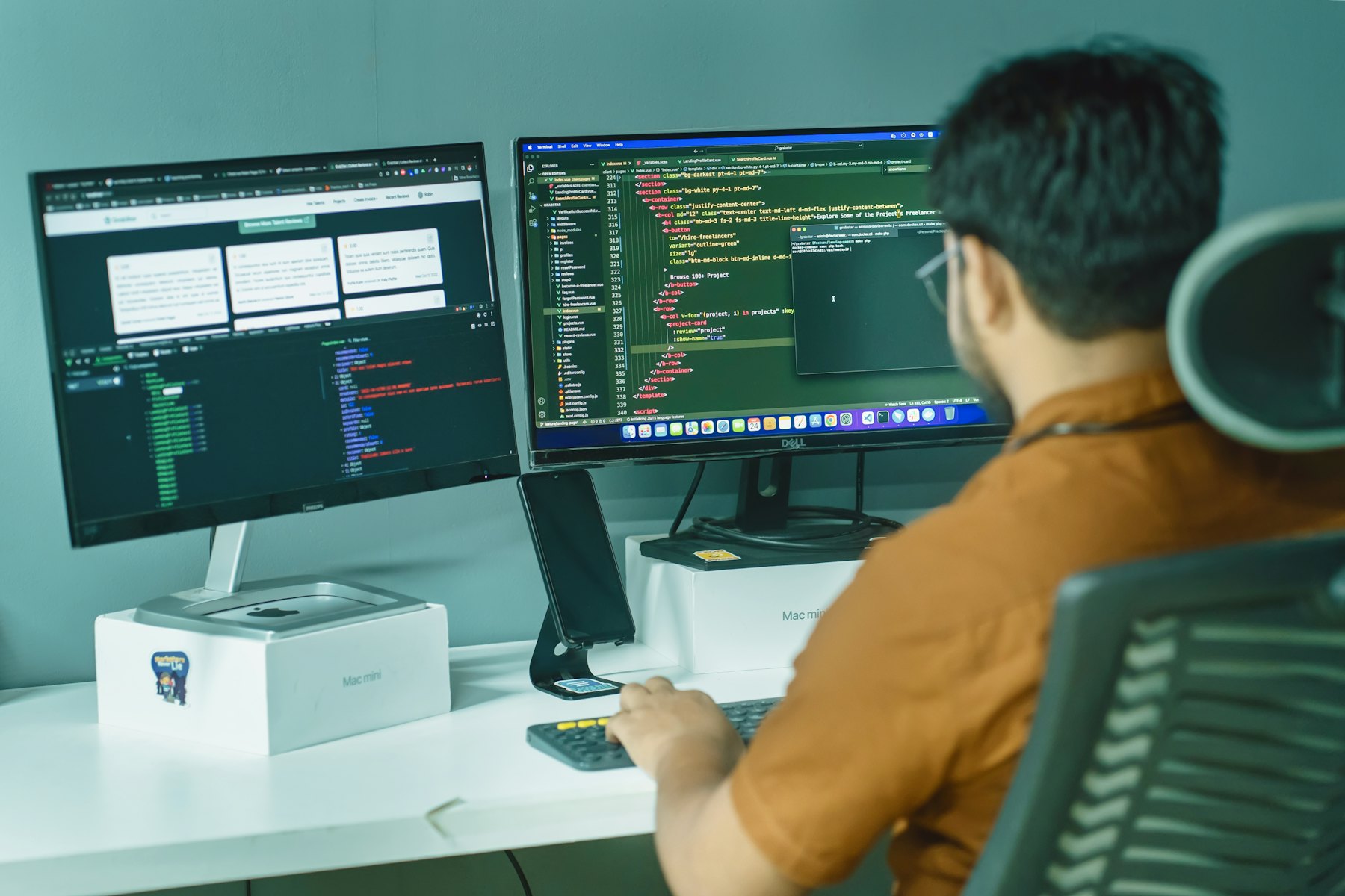 A man works across two monitors, a spreadsheet on one and code on the other