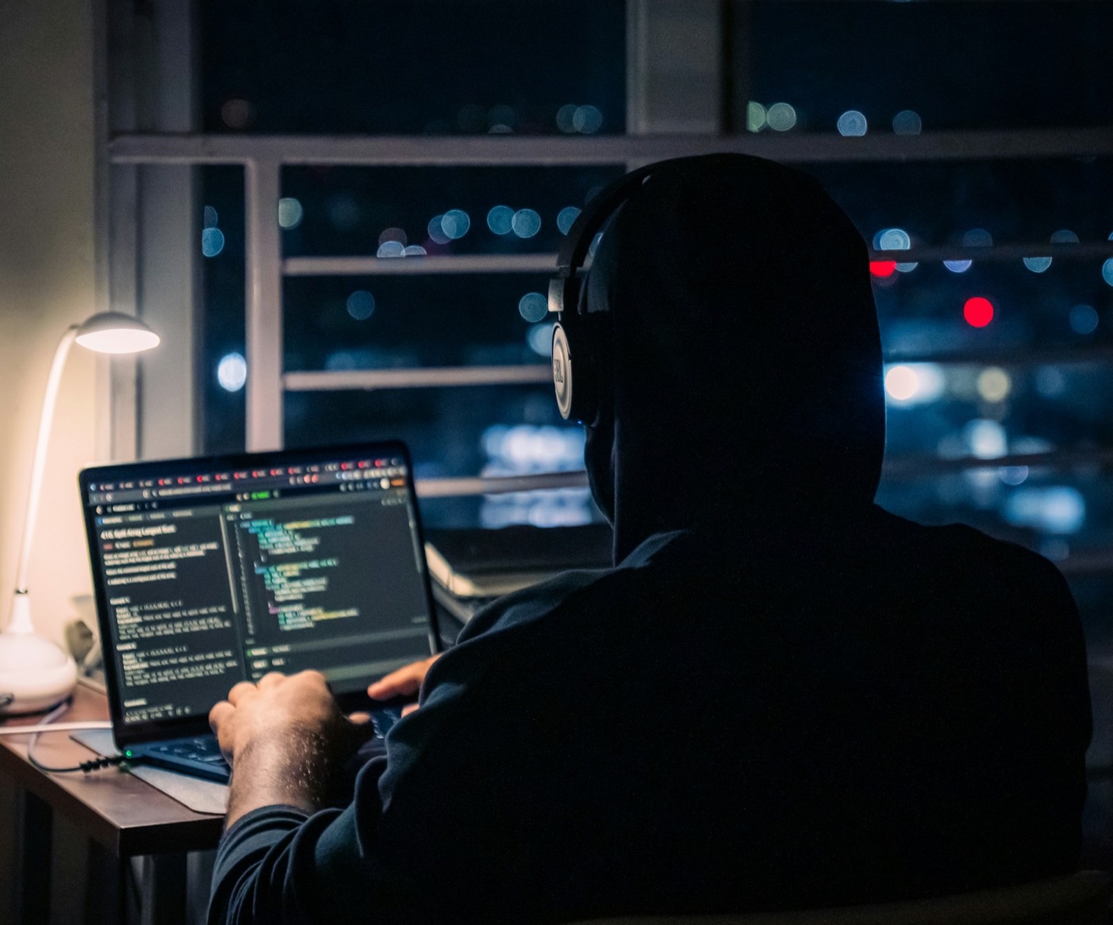 An engineer working at a laptop in a dark office, screen light on their face