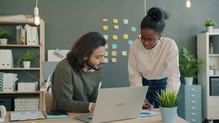 Four colleagues gathered around a desktop screen, one pointing at the work under discussion