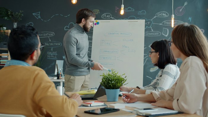 A team gathered around a whiteboard while a colleague walks through a plan