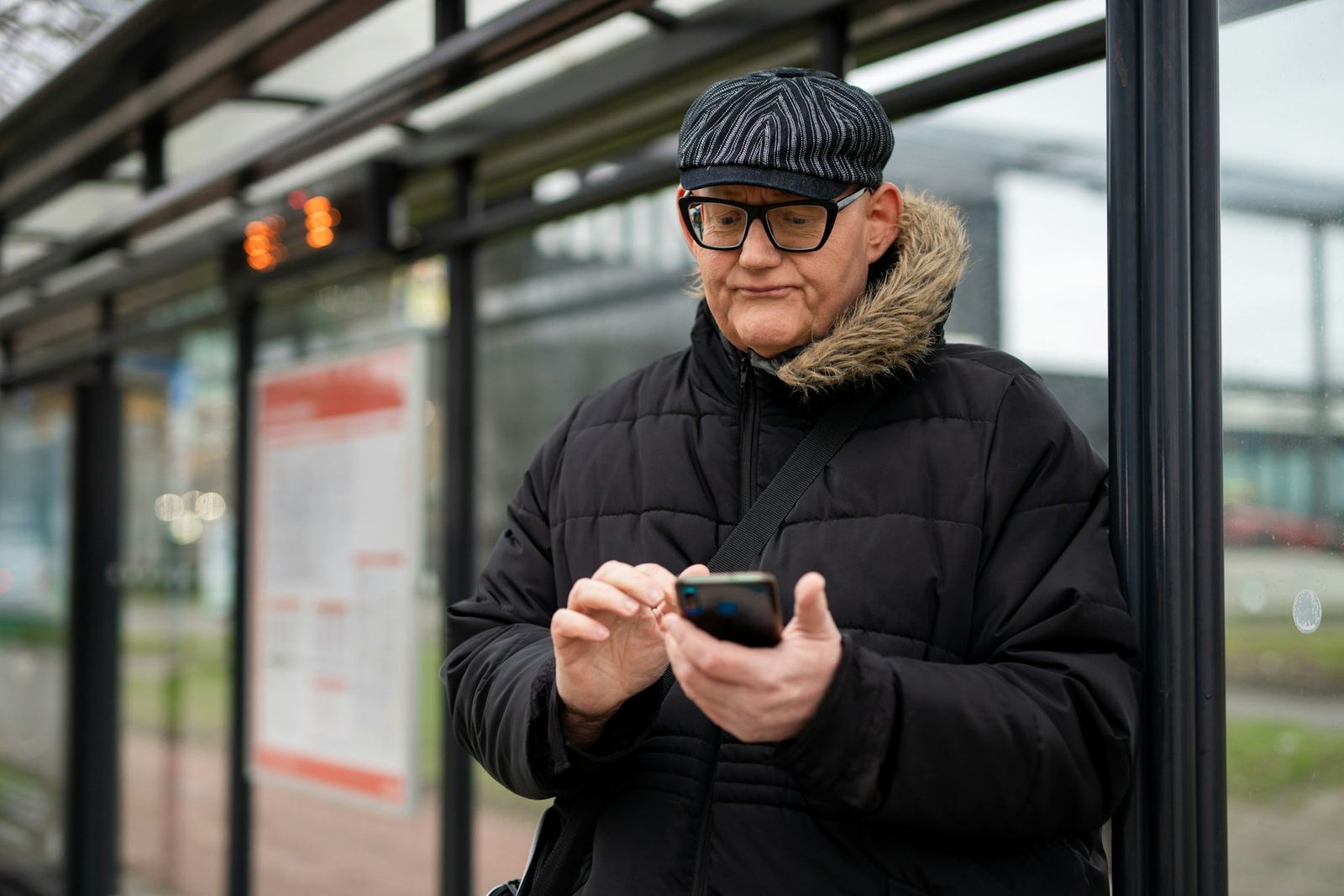 An older man at a bus stop reading his phone with the text enlarged