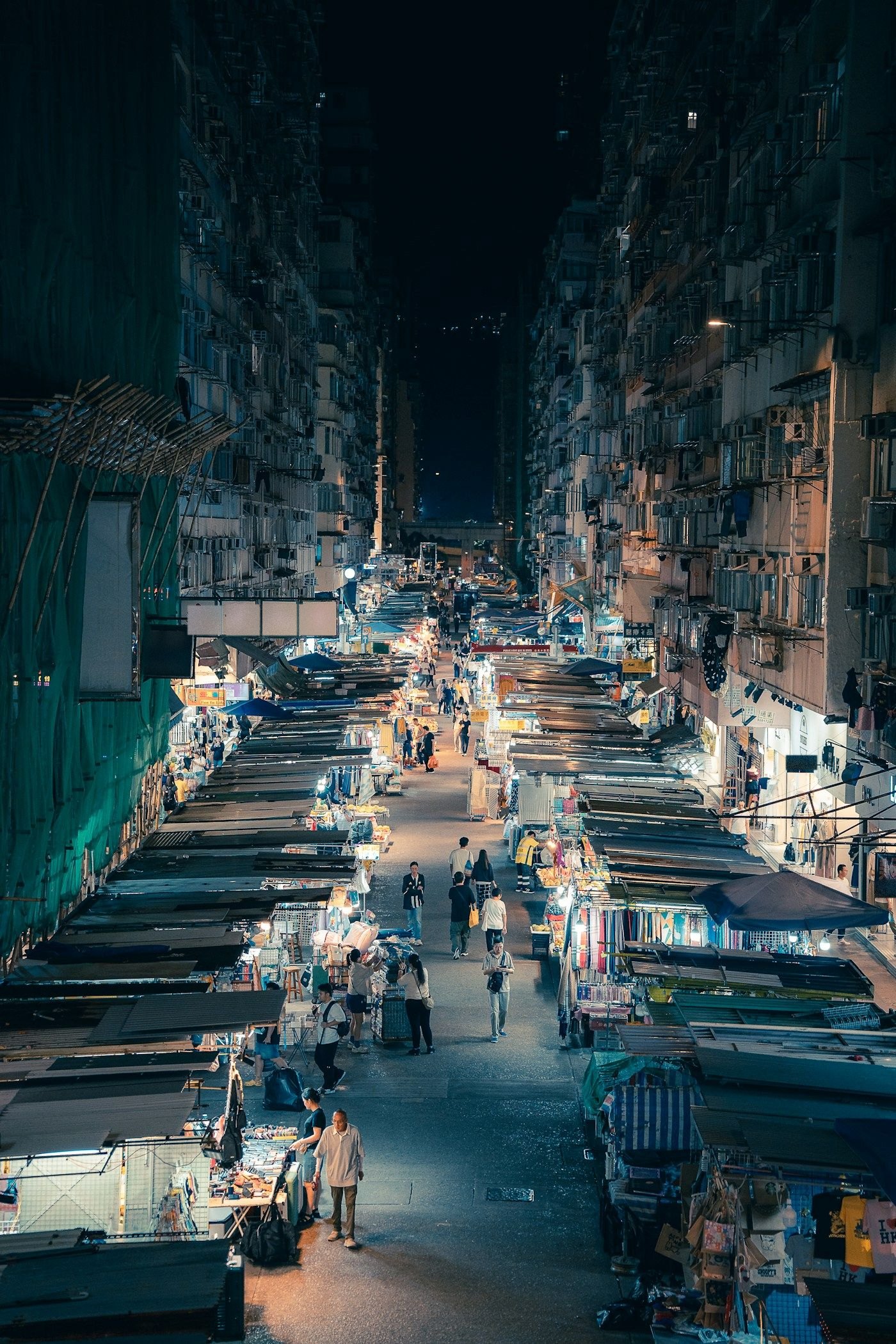 A night market seen from above, its long street lined with lit stalls between tall apartment blocks.
