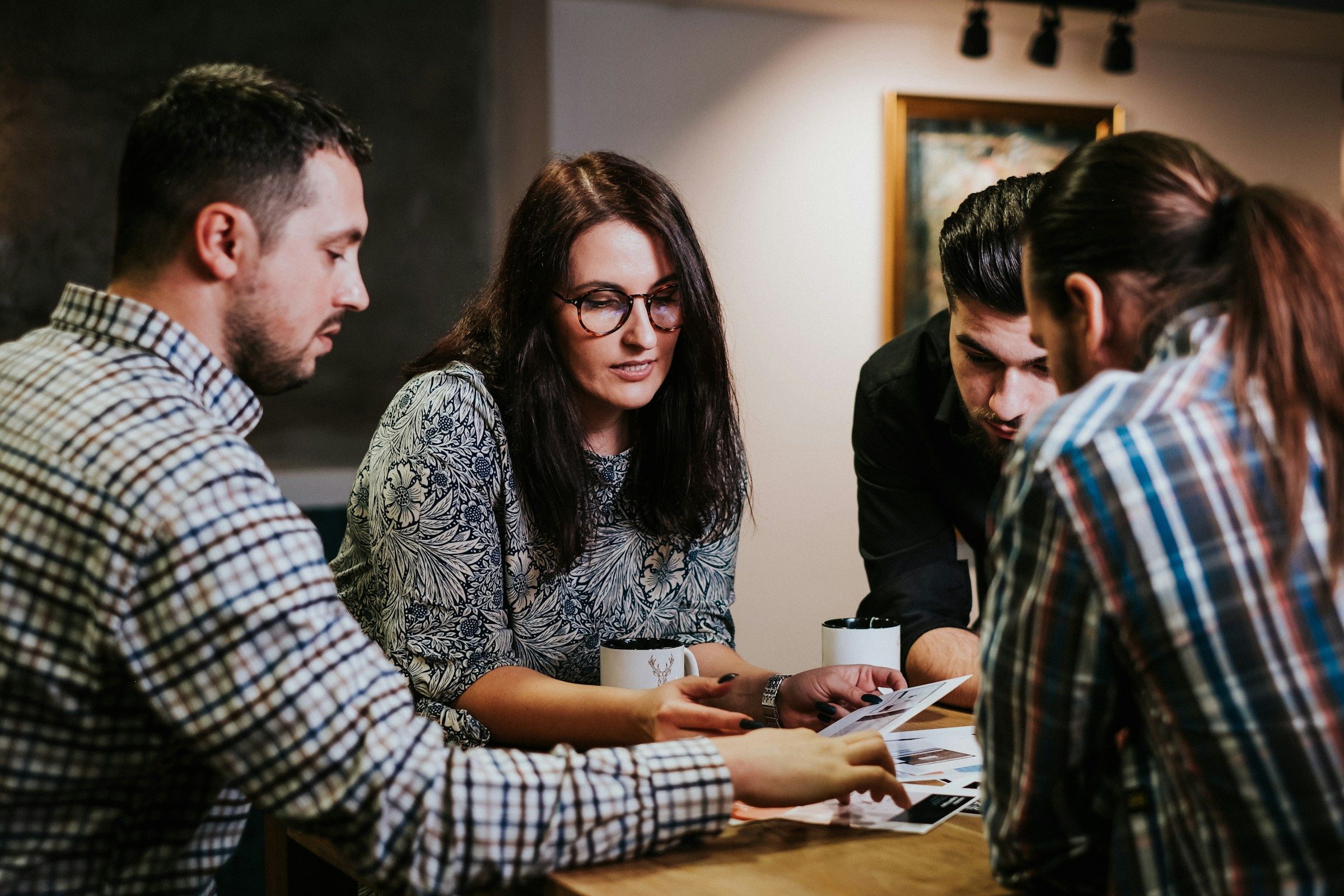 Four colleagues lean over printed pages on a wooden table, one pointing at a detail.