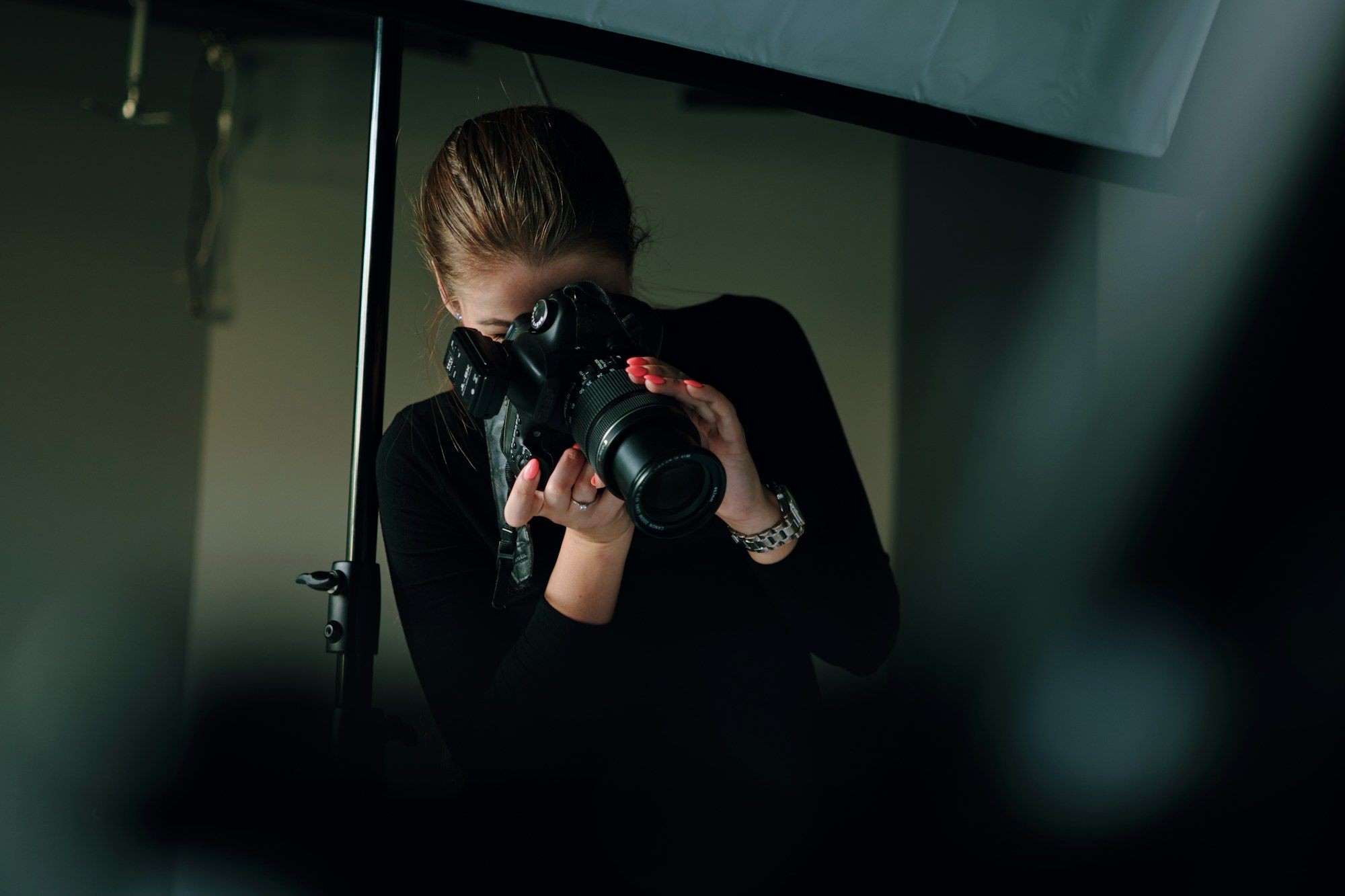 A photographer in black frames a shot through a camera in a dim studio.