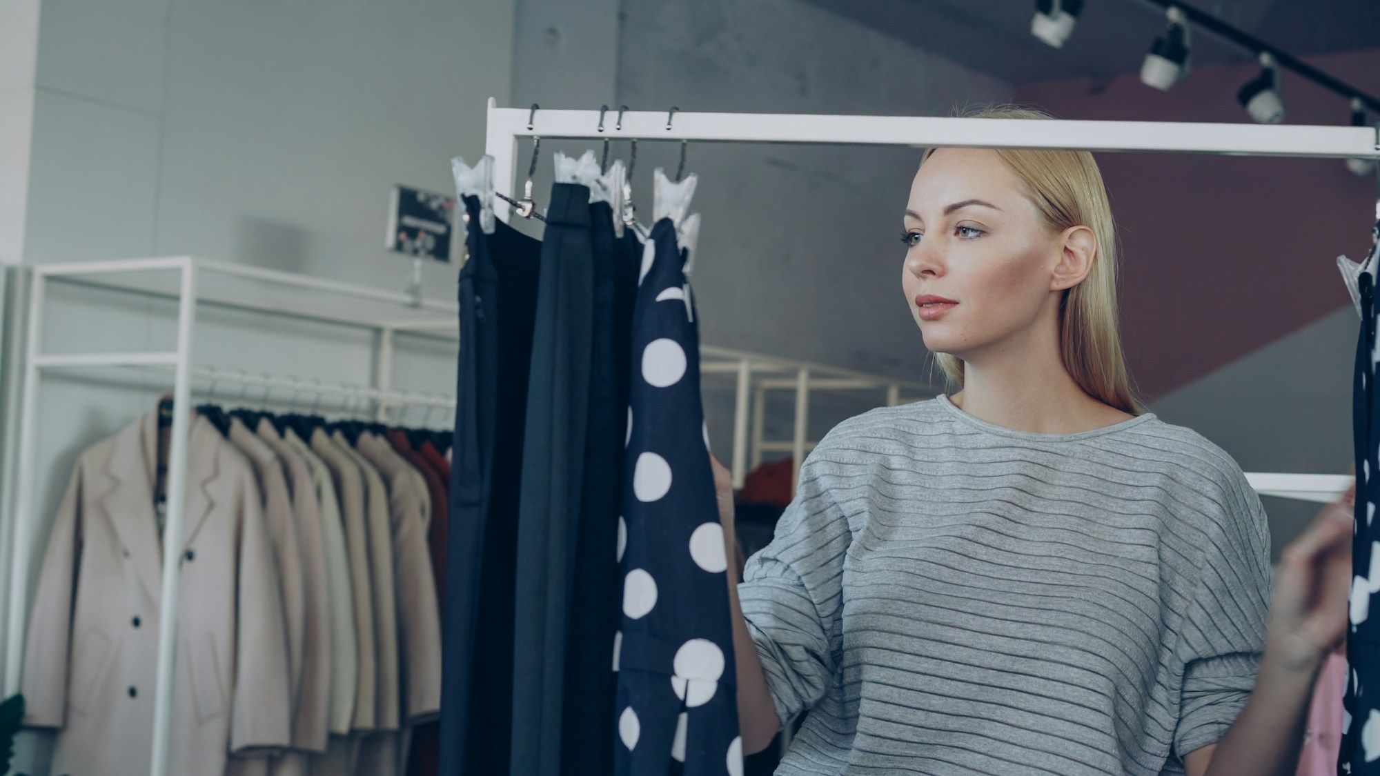 A woman looks along a clothing rail in a bright store, a polka-dot dress in the foreground.