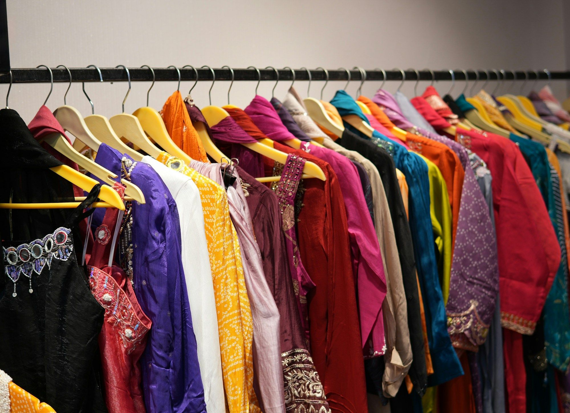 A rail of brightly coloured garments on yellow hangers in purple, orange, red and teal.